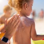 Caring mother apply sunblock to the back of her little daughter. Summer vacation sea beach