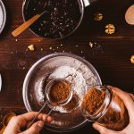 Female's hands sift cocoa powder into bowl