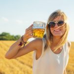 Happy girl holding beer glass in a big wheat-field.