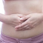 Young woman with abdominal pain at white background