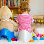 Closeup of cute little 12 months old toddler baby girl child sitting on potty. Kid playing with big plush soft toy. Toilet training concept. Baby learning, development steps