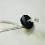 Far passare il nastrino attraverso i buchi del bottone.