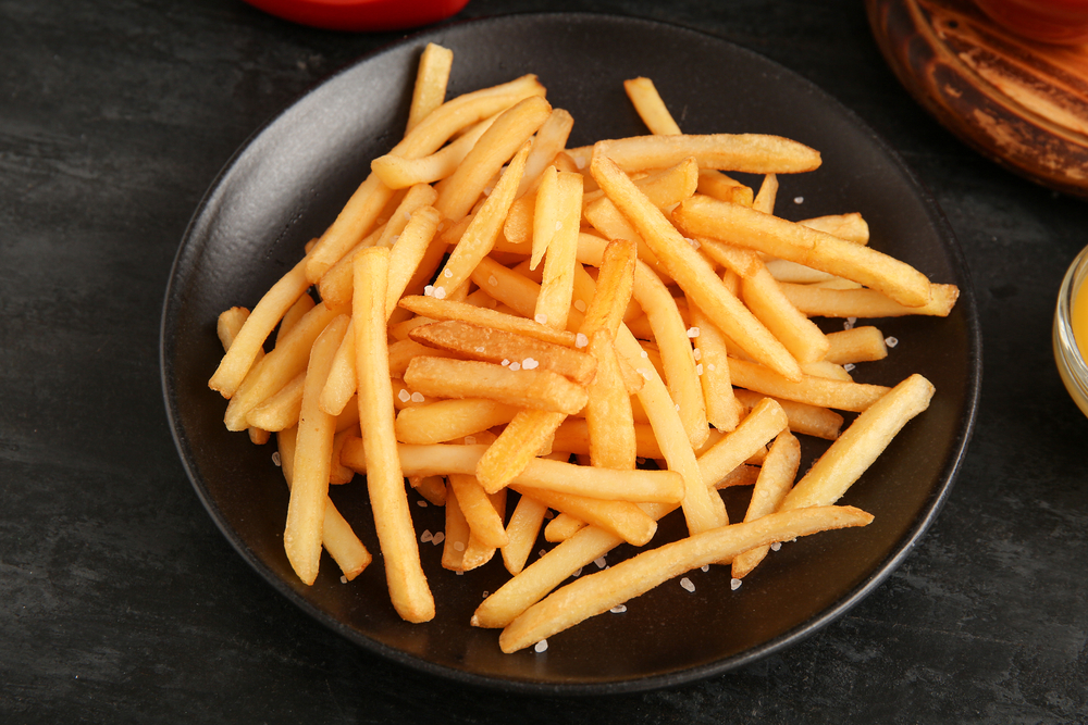 Plate with tasty french fries on grunge black background