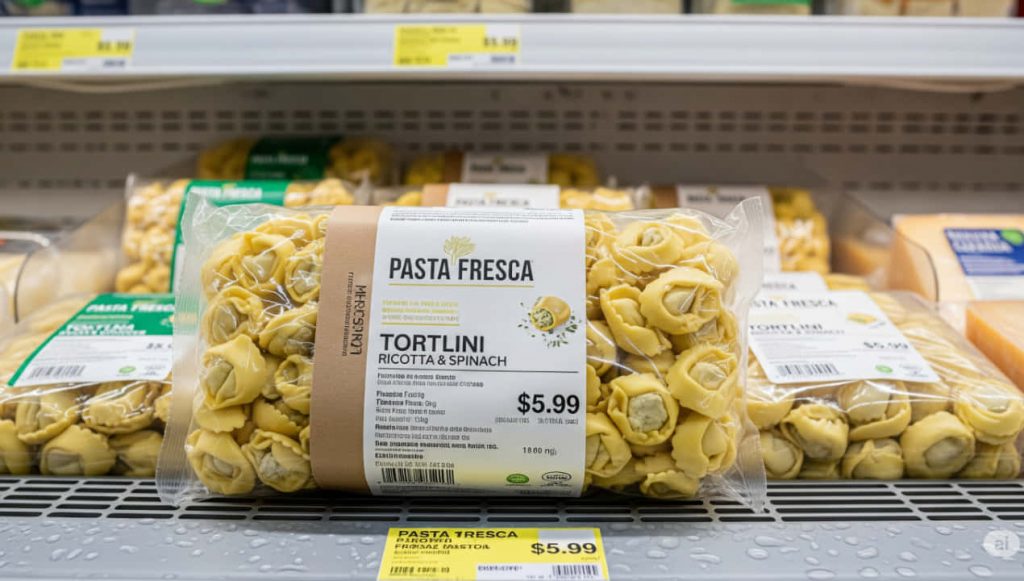 Una confezione di pasta fresca ripiena in primo piano su un banco frigo di supermercato.